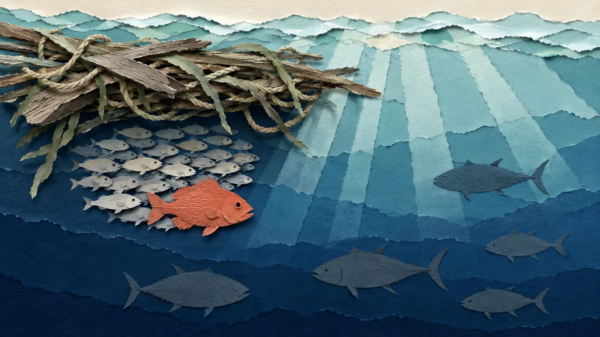 Illustrazione papercut di mare aperto estivo visto da sotto la superficie: un banco di pesci chiari raccolto all'ombra di un ammasso di legni e cime galleggianti, un piccolo pesce arancione in mezzo a loro e le grandi sagome scure di tonni e ricciole che passano nel blu sullo sfondo
