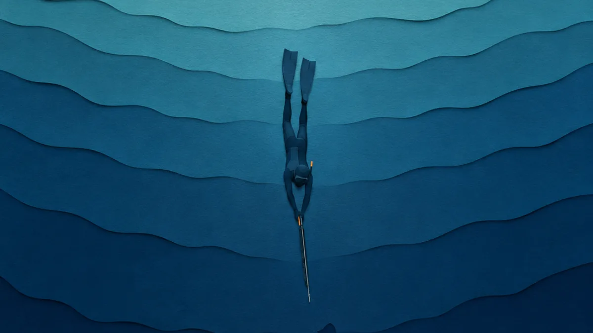 Illustrazione papercut di una discesa in apnea lungo fasce di mare che scuriscono, il subacqueo piccolo in basso su una secca profonda e la superficie lontana in cima